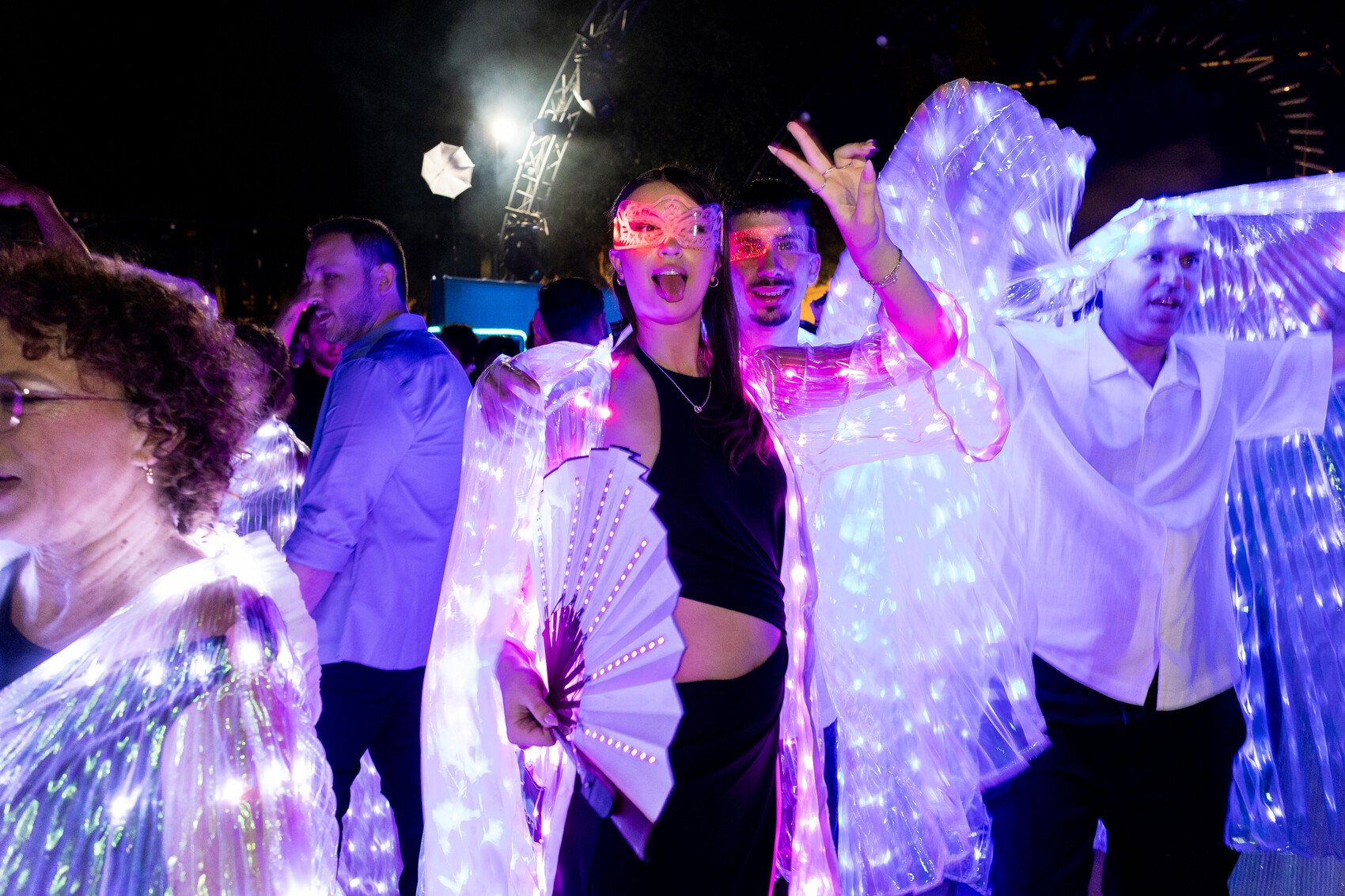 Guests dancing together in illuminated garments with a glowing fan and glasses